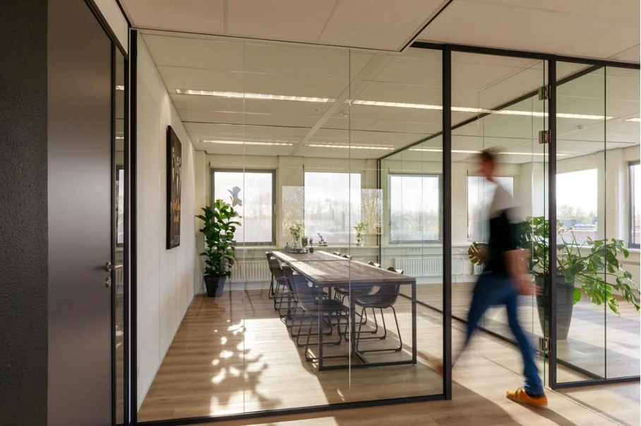 Vergaderruimte met glazen wanden aan de Baarnsche Dijk, met een persoon die langsloopt.